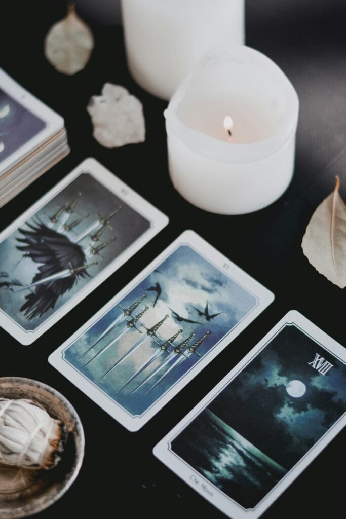 A calming tarot spread with three illustrated cards, white candles, crystals, and sage on a dark surface, used to support intuitive guidance, emotional clarity, and nervous system regulation