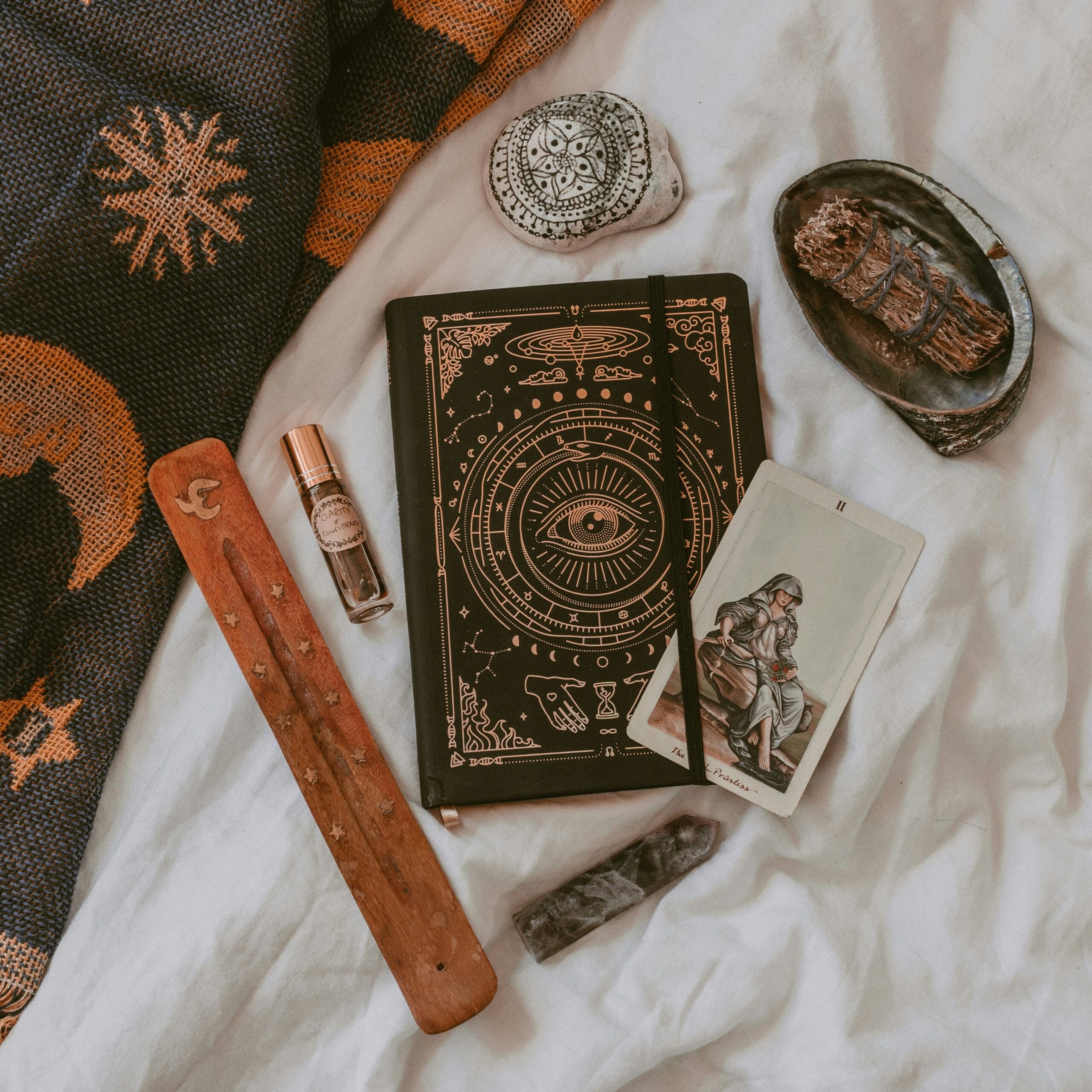 A flat lay of a tarot card alongside a mystical journal, crystals, sage, and essential oil on soft bedding, highlighting how tarot can support nervous system regulation, intuitive healing, and grounding practices